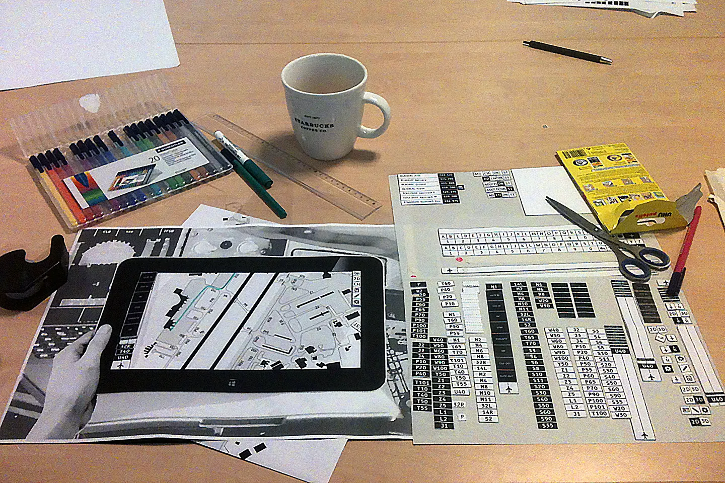 A paper prototype of the map app on a tablet over printed airport charts, mid build of the interface