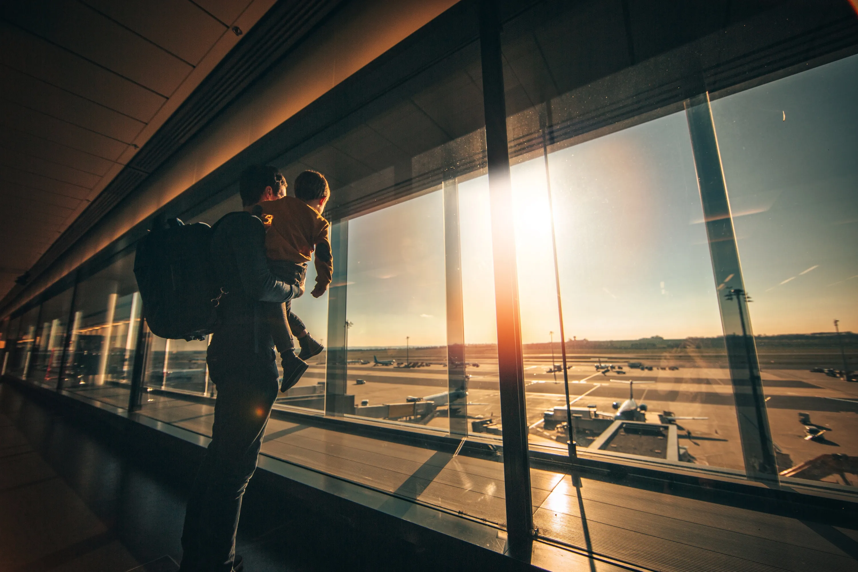 A parent holding a child at an airport window at sunset, the journey moments a companion app travels through