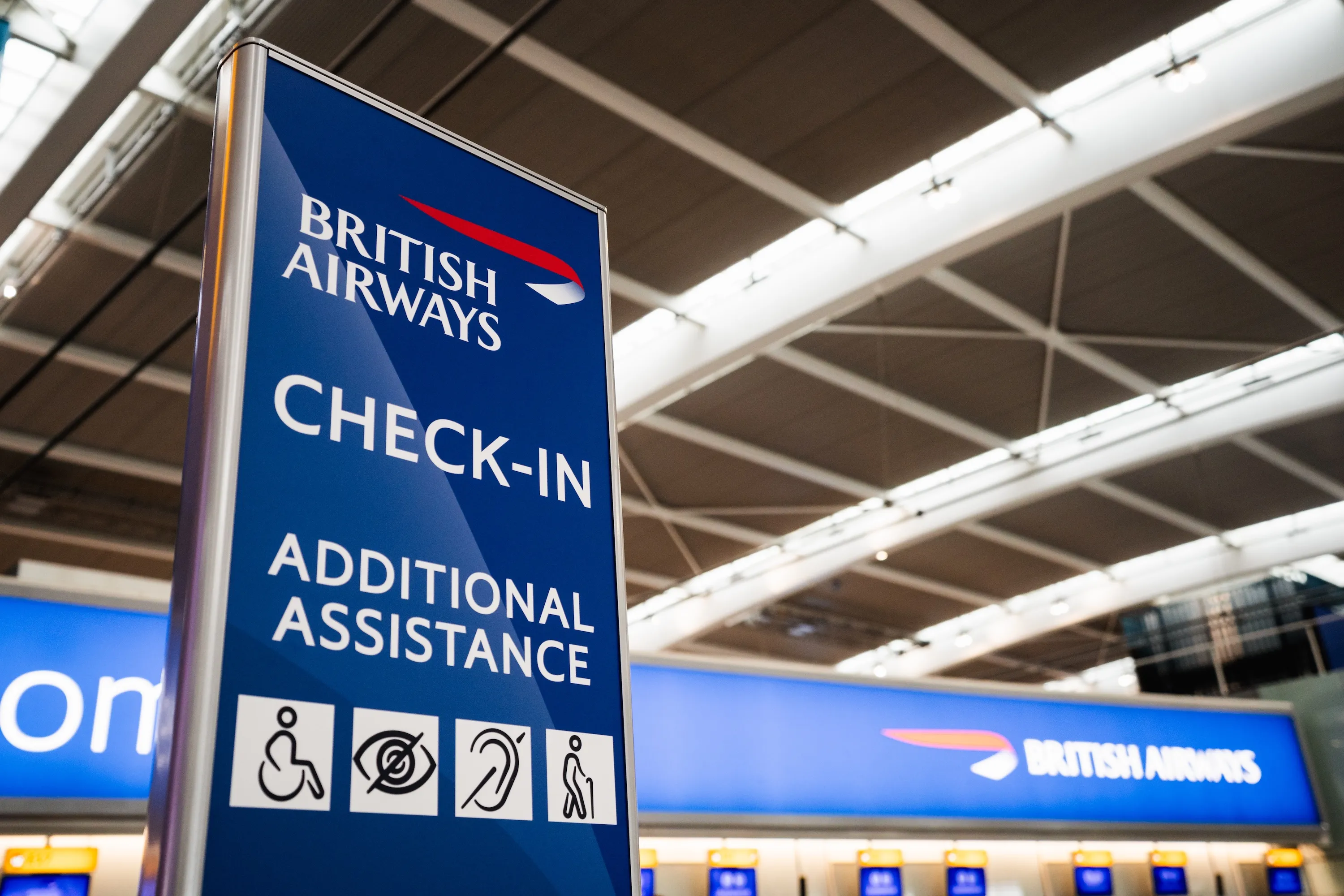 A British Airways check-in and additional assistance sign with accessibility icons, at the airport